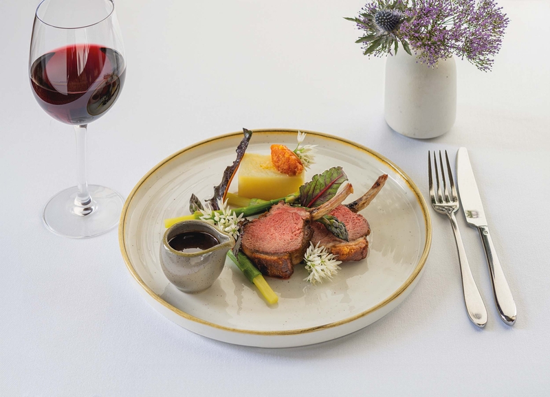 a plate of lamb cutlets on a linen cloth with red wine and flowers