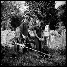 Cemetery workers with tools, leaning against a tombstone