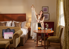 A bride holds her wedding dress up in a hotel bedroom